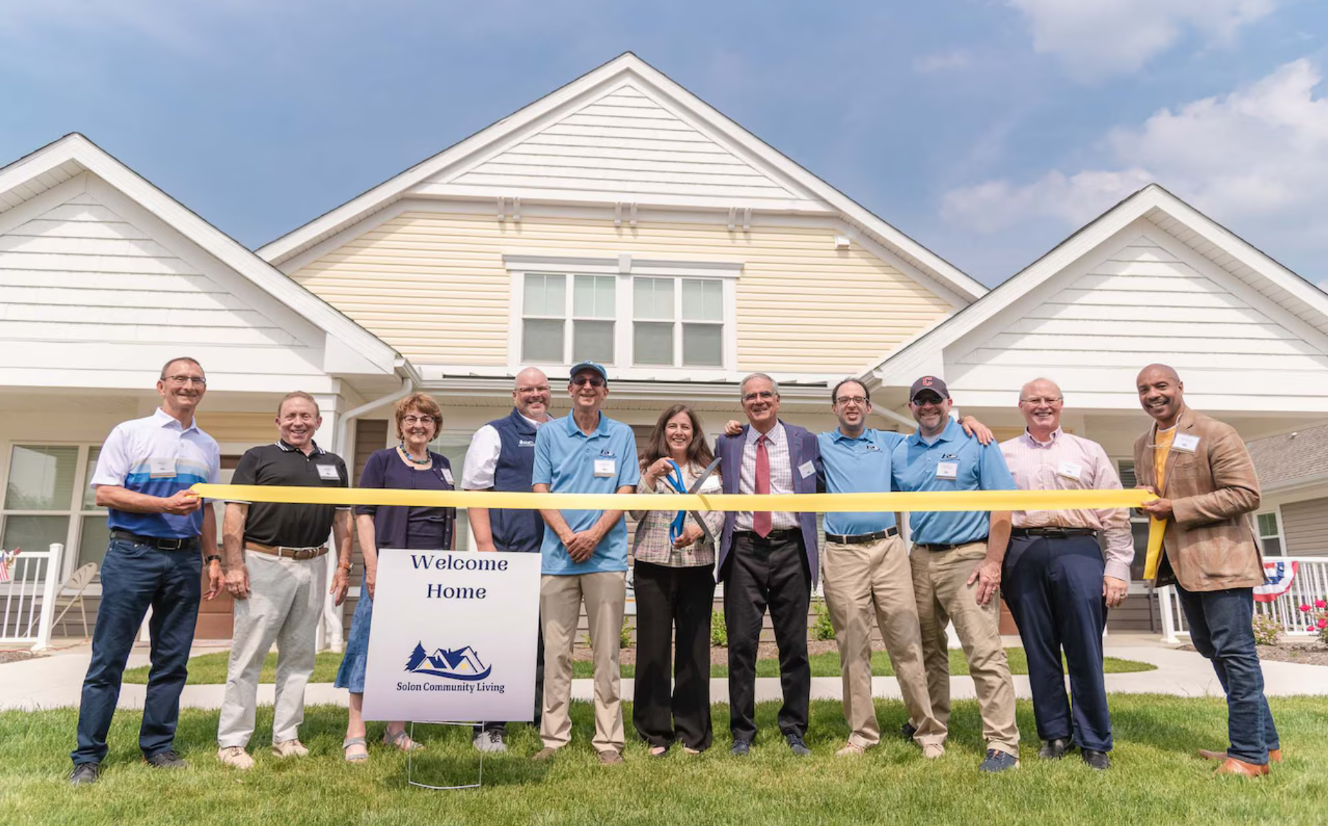 People cutting ribbon in front of homes