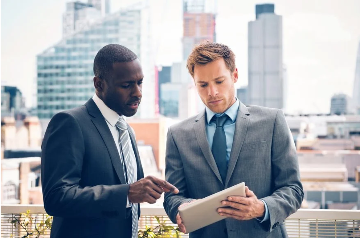 Two men in suits reviewing tablet on rooftop